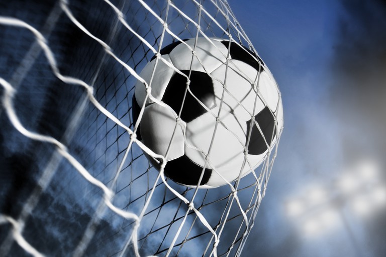 Football Hitting Goal Net Against Blurred Floodlight