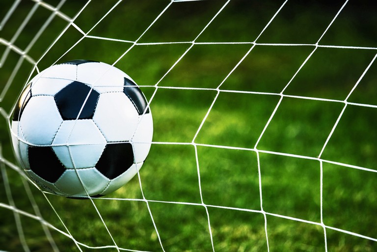 Football Hitting Goal Net Against Grass Pitch
