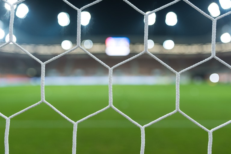 Blurred Pitch and Stadium Through Goal Net